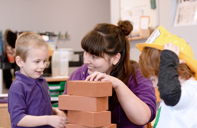 Nursery practitioner helping a child stack building blocks