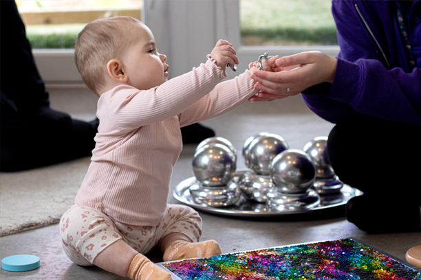 Baby sitting up and handing an item to an adult