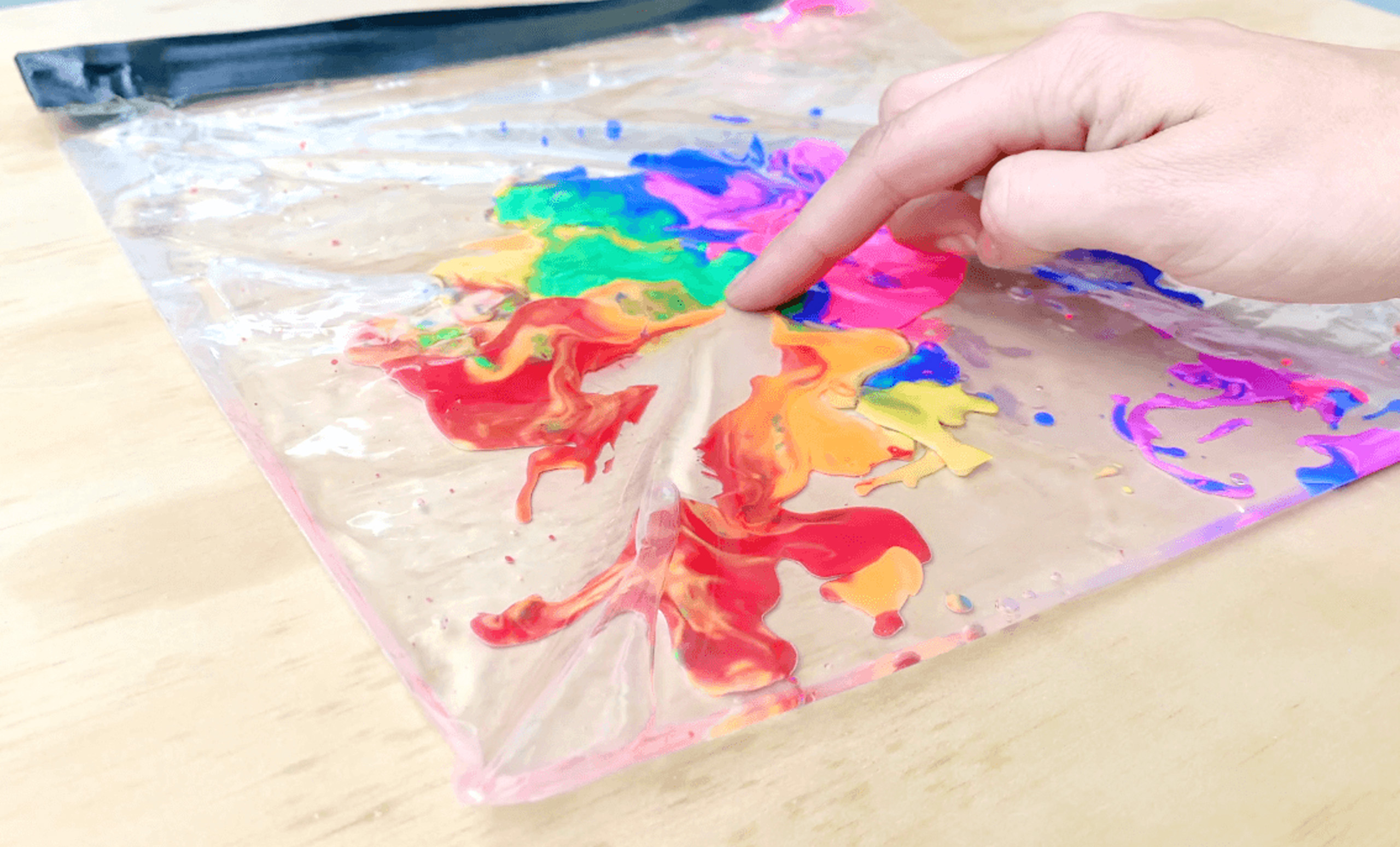 Child’s hand exploring multicoloured paint inside a sealed ziplock bag